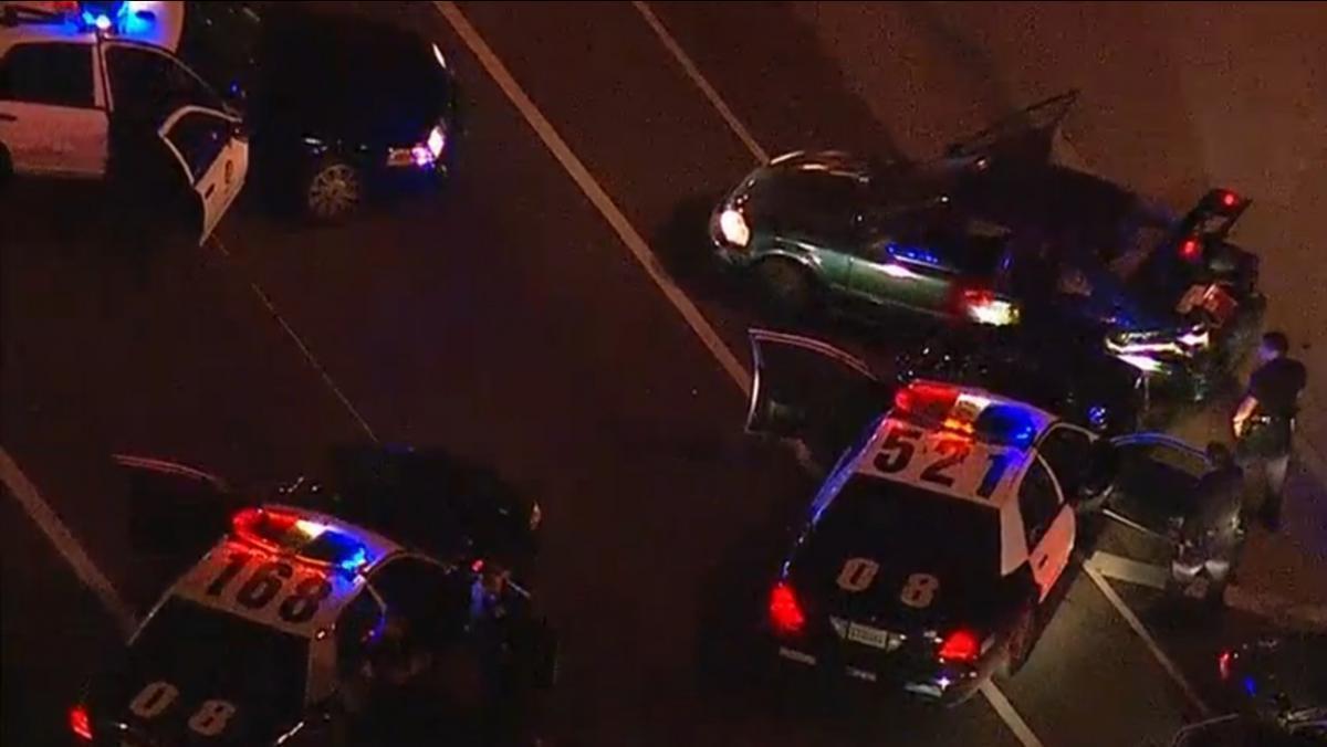 Multiple police officers contacting persons on the street, with a police vehicle’s emergency lights